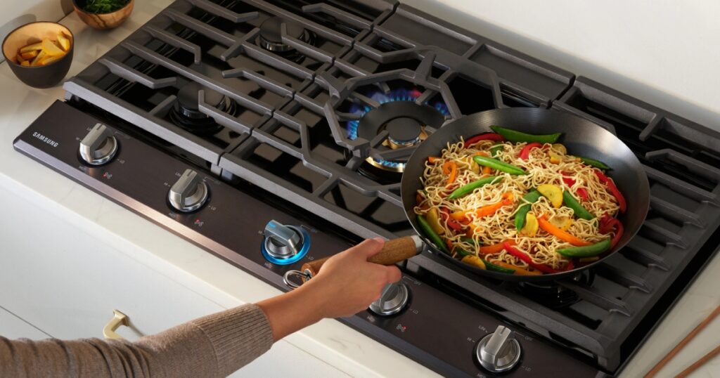 Samsung gas cooktop with uneven heating—one burner burning stronger than the other while stir-frying vegetables in a wok. Common causes include burner clogs, gas flow issues, or faulty ignition. Learn how to troubleshoot and fix uneven heat distribution on your Samsung cooktop